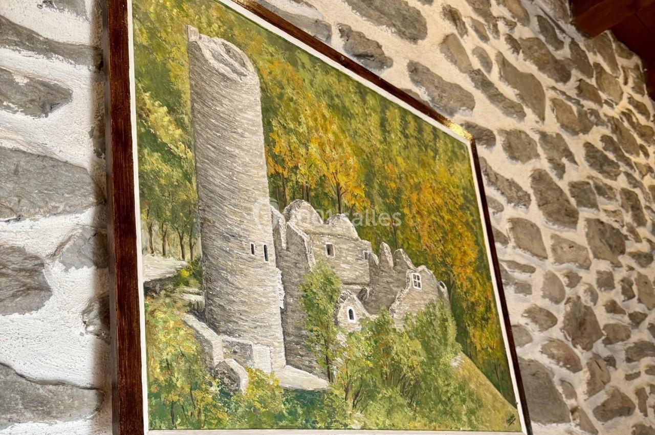 Peinture représentant une tour en pierre et des ruines entourées de végétation, accrochée sur un mur en pierre.