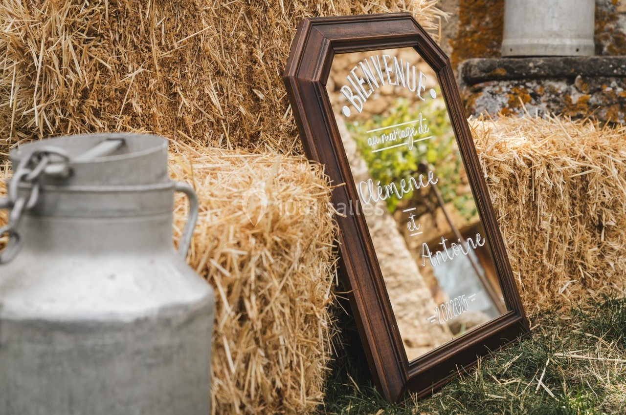 Miroir encadré avec un message de bienvenue posé contre des bottes de paille, à côté d'un bidon en métal.