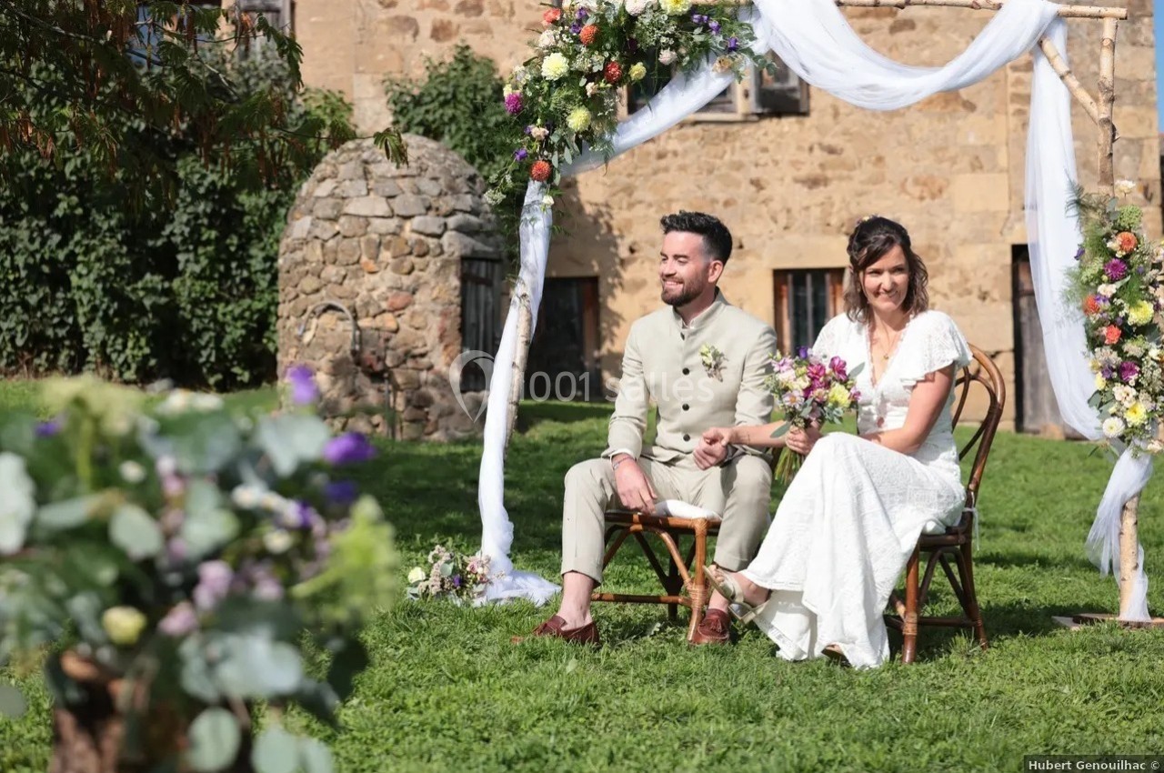 Un couple assis lors d'une cérémonie de mariage en extérieur, entouré de décorations florales et de voiles blancs.