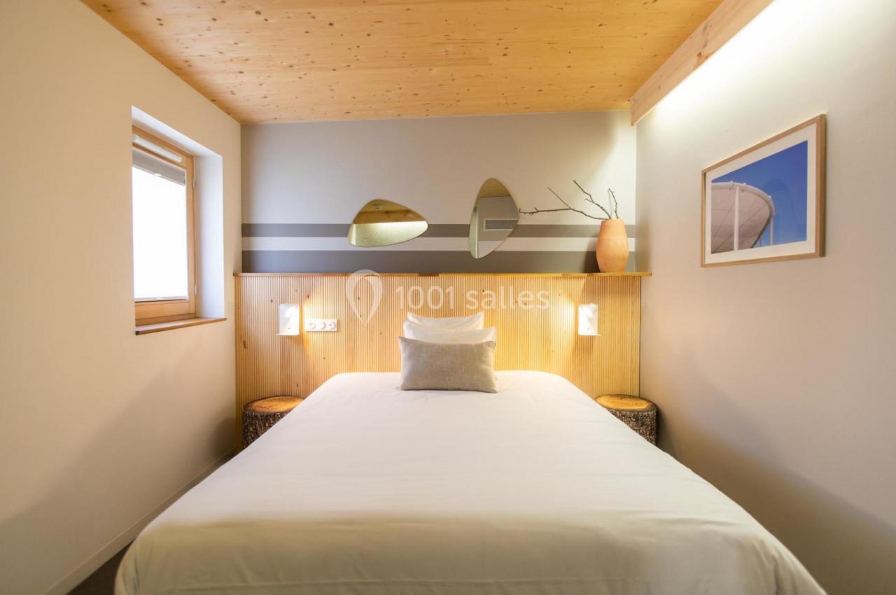 Chambre lumineuse avec lit double, mur en bois, décor minimaliste et fenêtre laissant entrer la lumière naturelle.