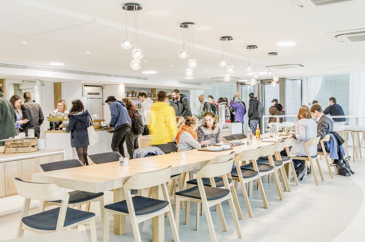 Personnes rassemblées dans un espace lumineux avec tables en bois, chaises et comptoirs de restauration.