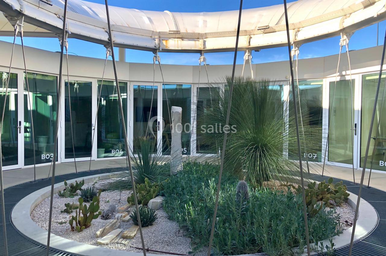 Jardin circulaire avec plantes succulentes et arbustes, entouré de baies vitrées et d'une structure métallique.
