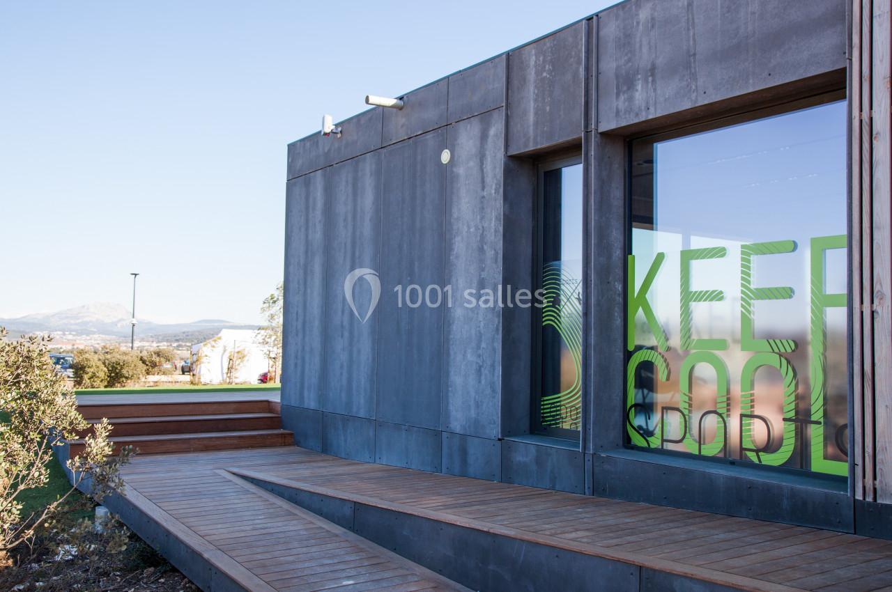 Façade d'un bâtiment moderne avec une grande baie vitrée affichant le message ’Keep Cool’, entourée de végétation.