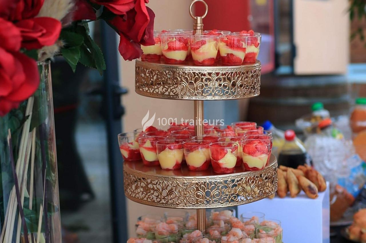 Présentoir doré à deux étages avec verrines de desserts aux fraises et verrines salées, entouré de décorations florales.