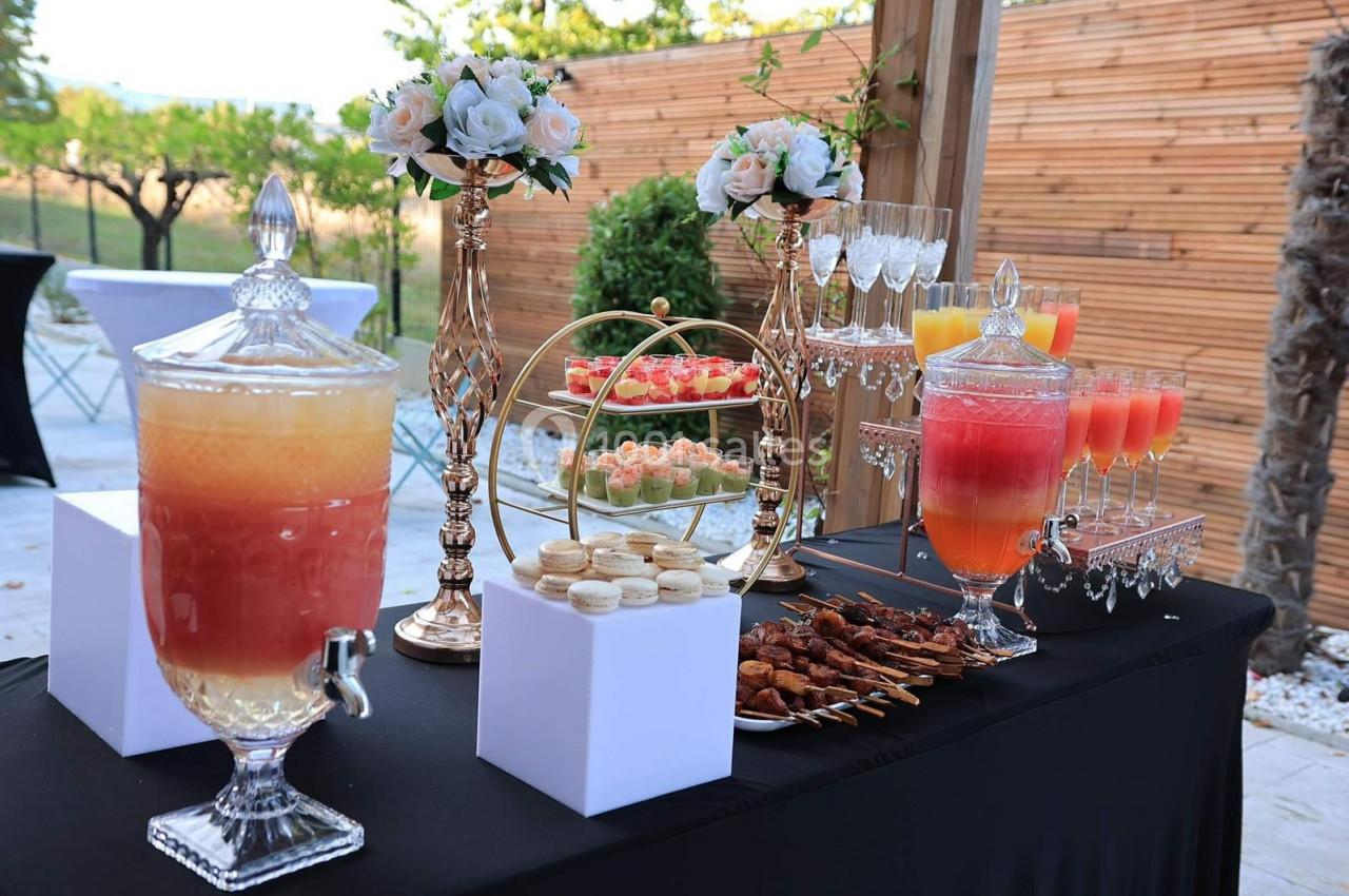 Table de réception en extérieur avec boissons, verrines, macarons, brochettes et décorations florales élégantes.