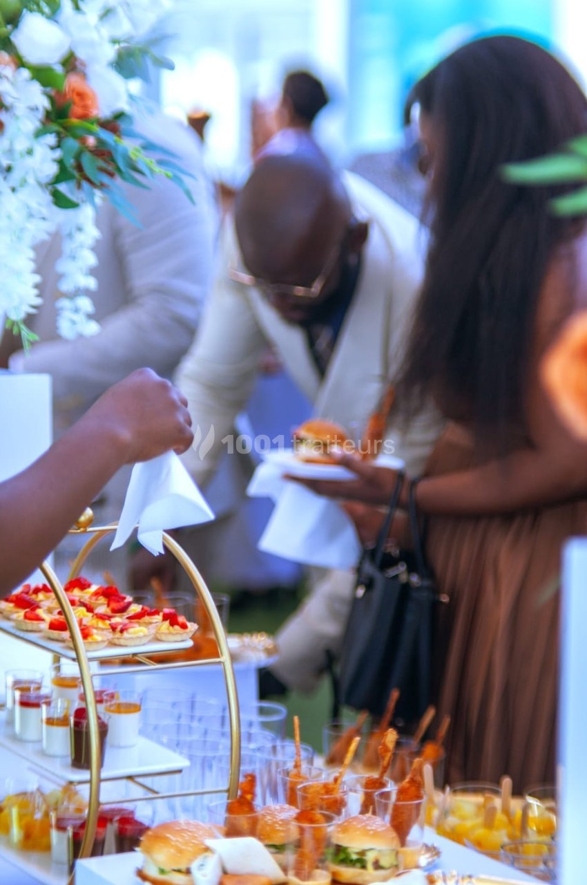 Personnes se servant à un buffet avec des plats variés, dont des verrines et des mini-burgers, dans un cadre élégant.