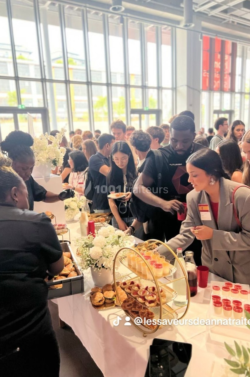 Des personnes se servent à un buffet garni de plats variés dans un espace lumineux avec de grandes baies vitrées.