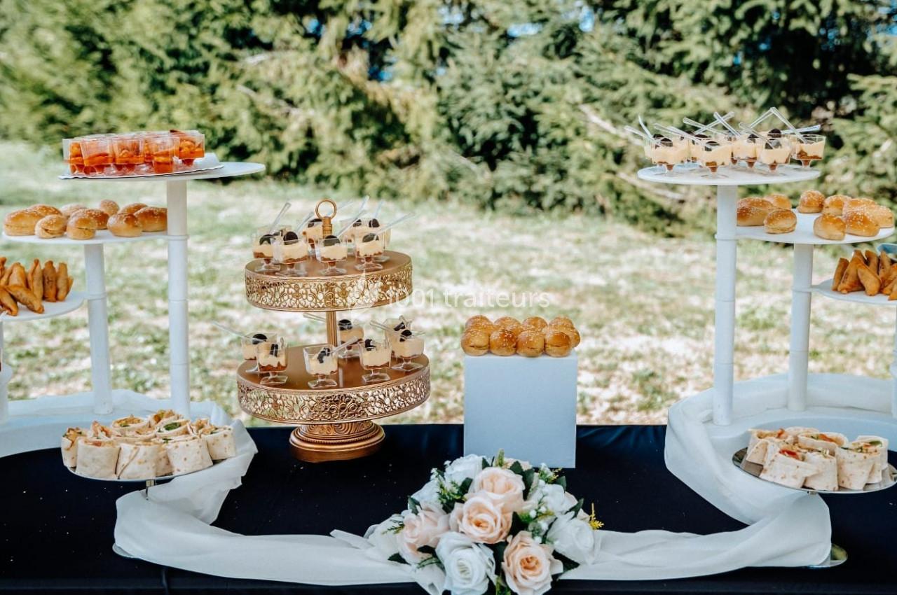Buffet en plein air avec des amuse-bouches variés disposés sur des présentoirs, décoré de fleurs blanches et roses.