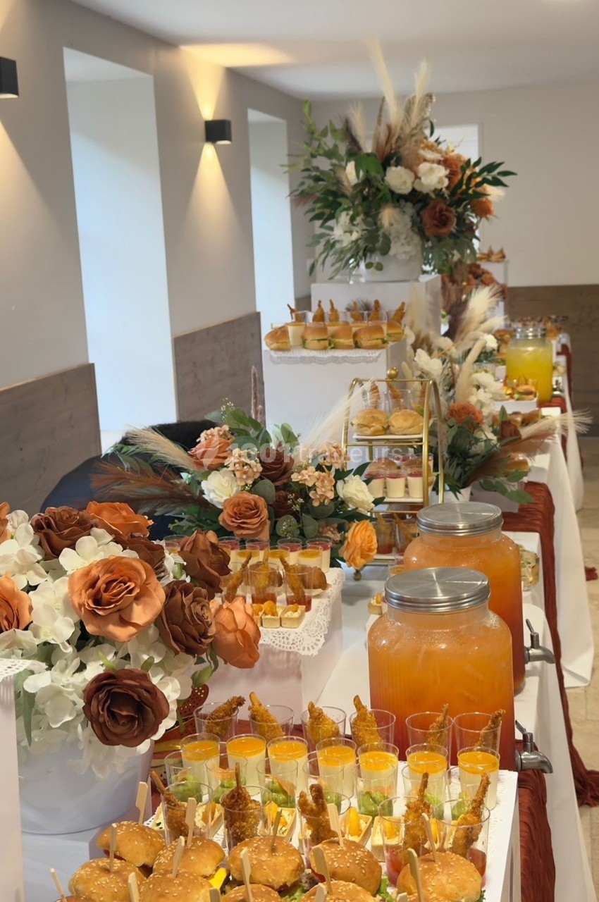 Buffet décoré avec des fleurs dans des tons chauds, proposant boissons, verrines et amuse-bouches variés.
