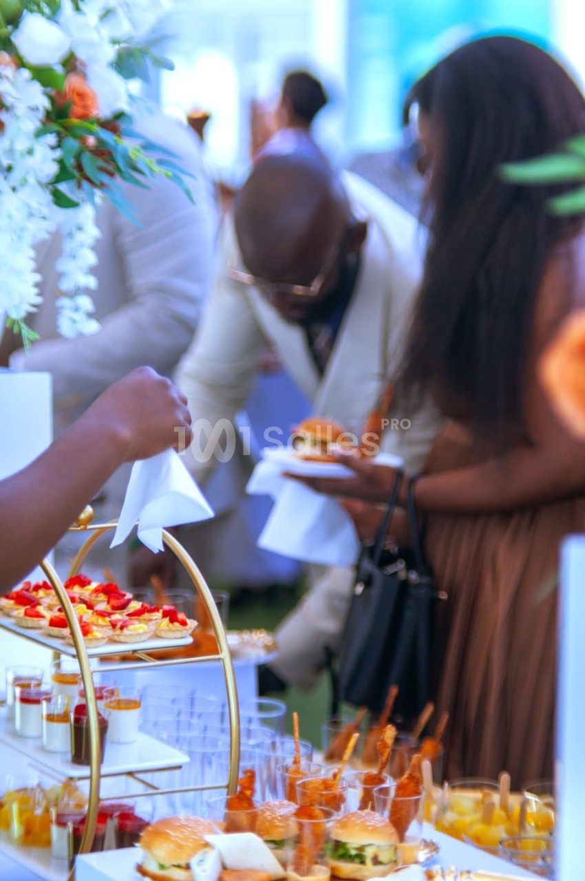 Personnes se servant à un buffet avec des plats variés, dont des burgers, verrines et desserts, dans un cadre élégant.