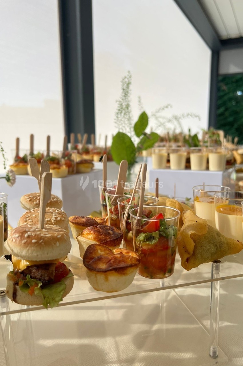 Buffet avec mini-burgers, verrines, samoussas et autres amuse-bouches disposés sur une table lumineuse.