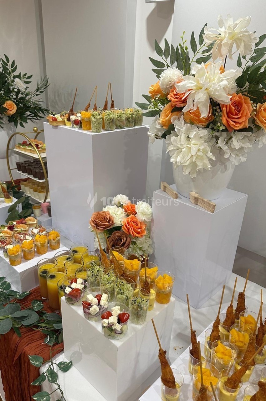 Buffet élégant avec verrines colorées, brochettes apéritives et décoration florale aux tons orange et blanc.