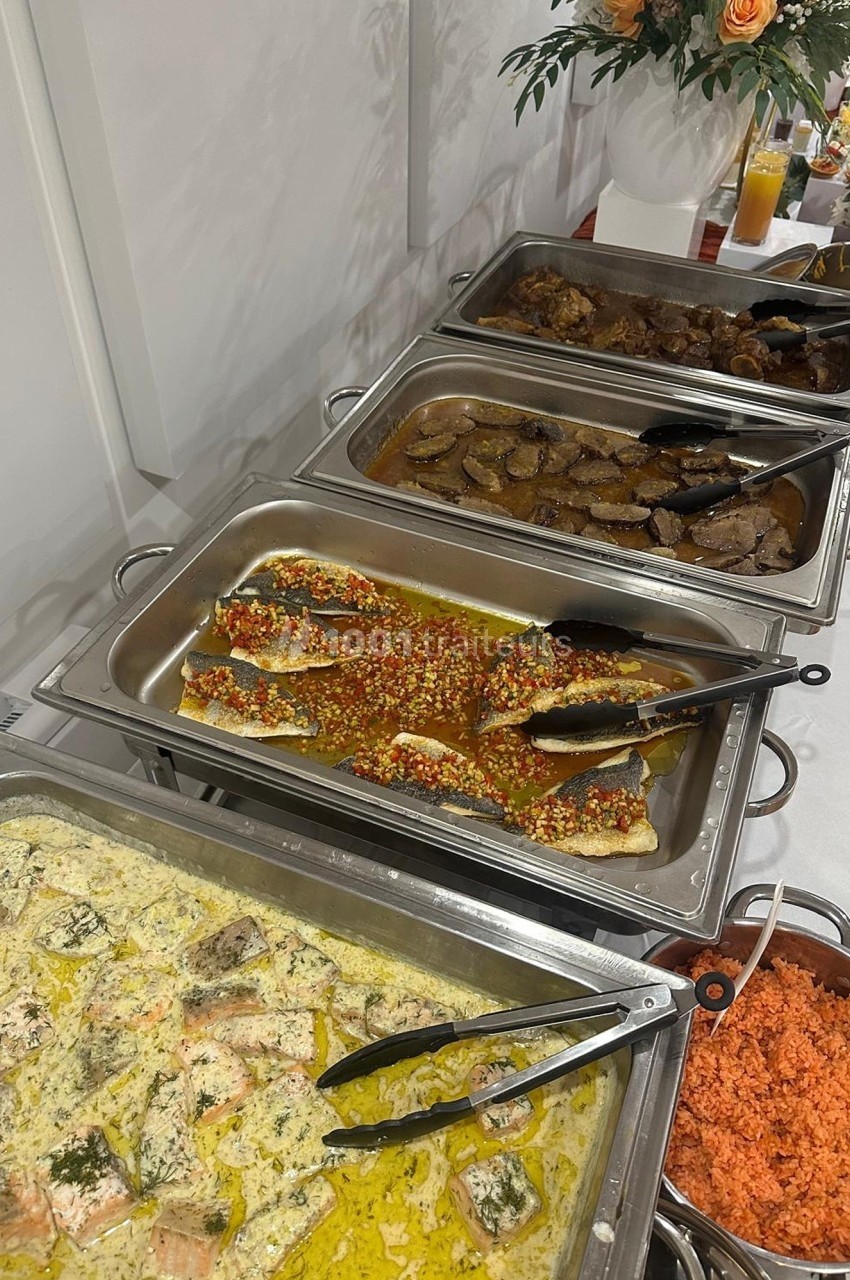 Buffet avec plats variés comprenant du poisson en sauce, de la viande, du riz et des légumes, présenté dans des plats en…