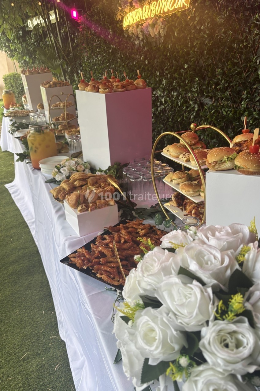 Buffet en plein air avec divers plats, boissons, fleurs blanches et décorations sur une table blanche.