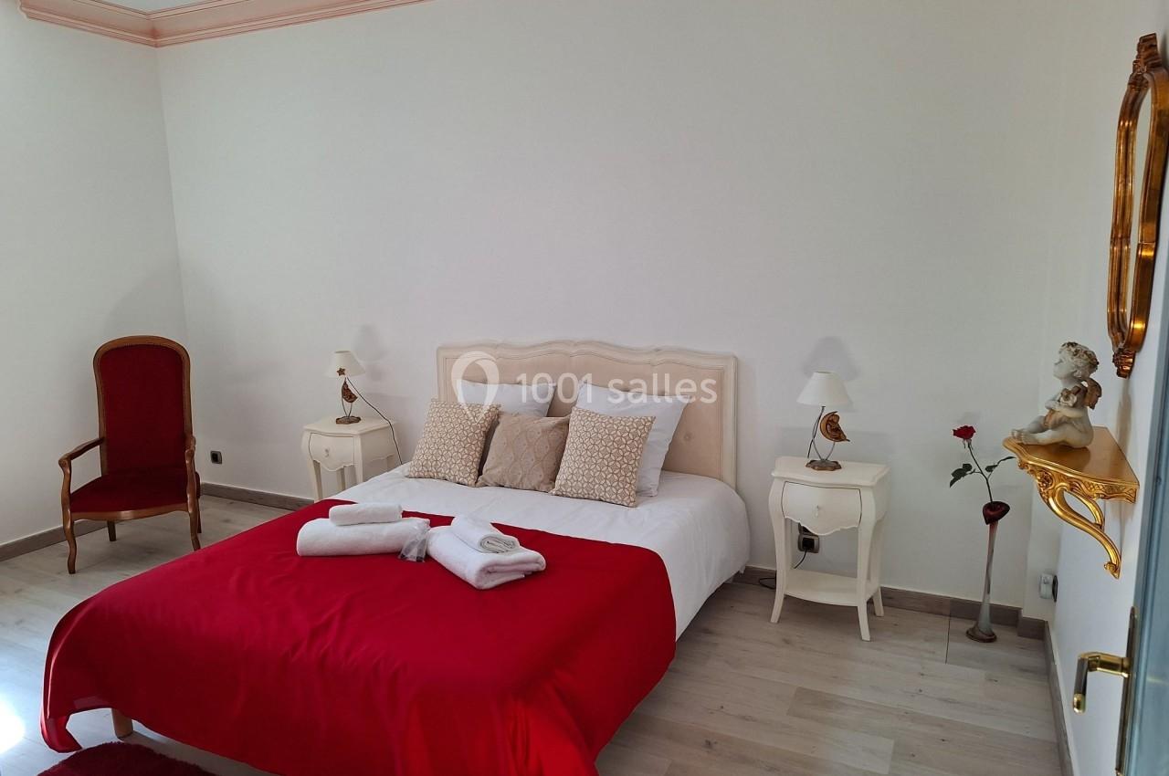 Chambre lumineuse avec un lit double, drap rouge, deux tables de chevet, une chaise et une décoration murale.