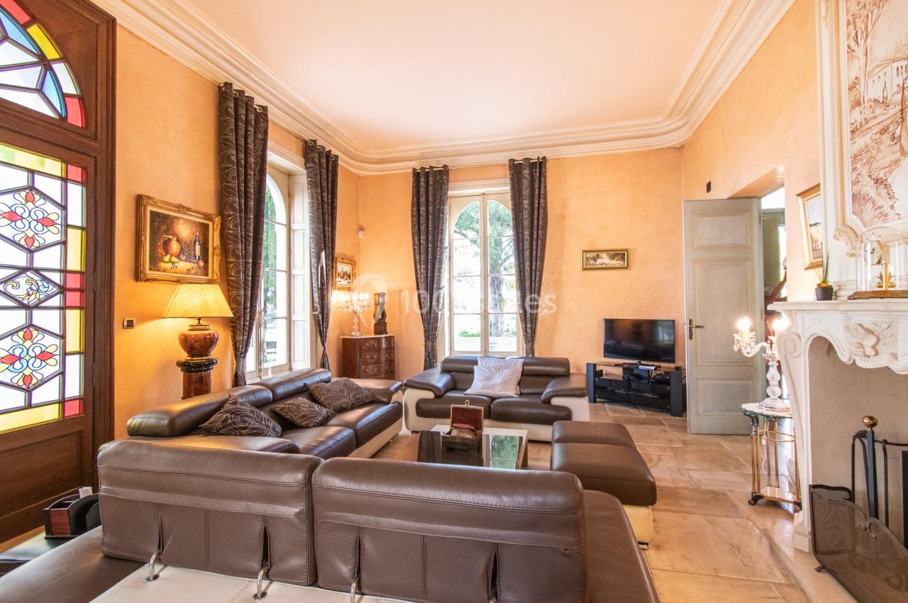 Salon élégant avec canapés en cuir, cheminée, vitraux colorés et grandes fenêtres laissant entrer la lumière naturelle.