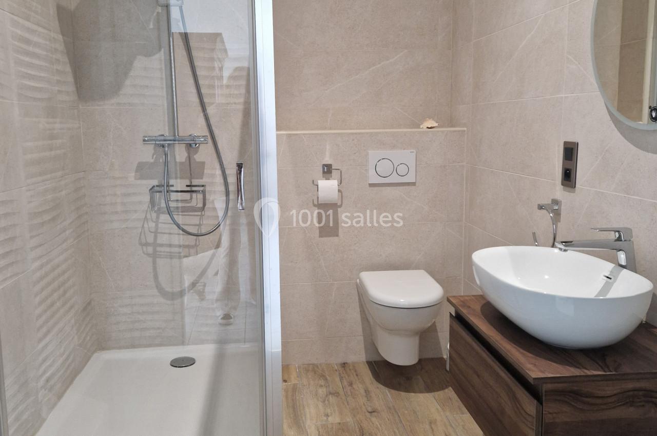 Salle de bain moderne avec douche à l'italienne, lavabo sur meuble en bois, toilettes suspendues et miroir rond.