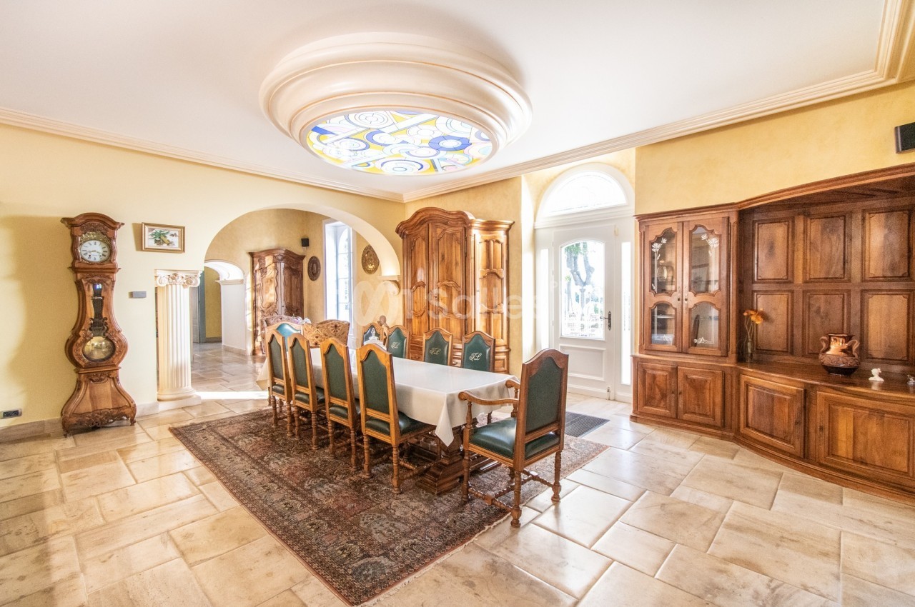 Salle à manger lumineuse avec une grande table entourée de chaises, meubles en bois et un plafond décoratif.
