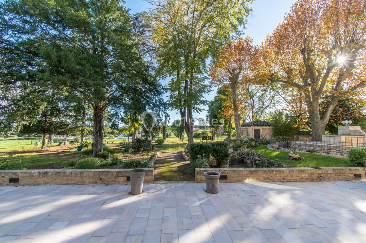 Terrasse en pierre donnant sur un jardin arboré avec pelouse, allées et arbres aux feuilles d'automne.