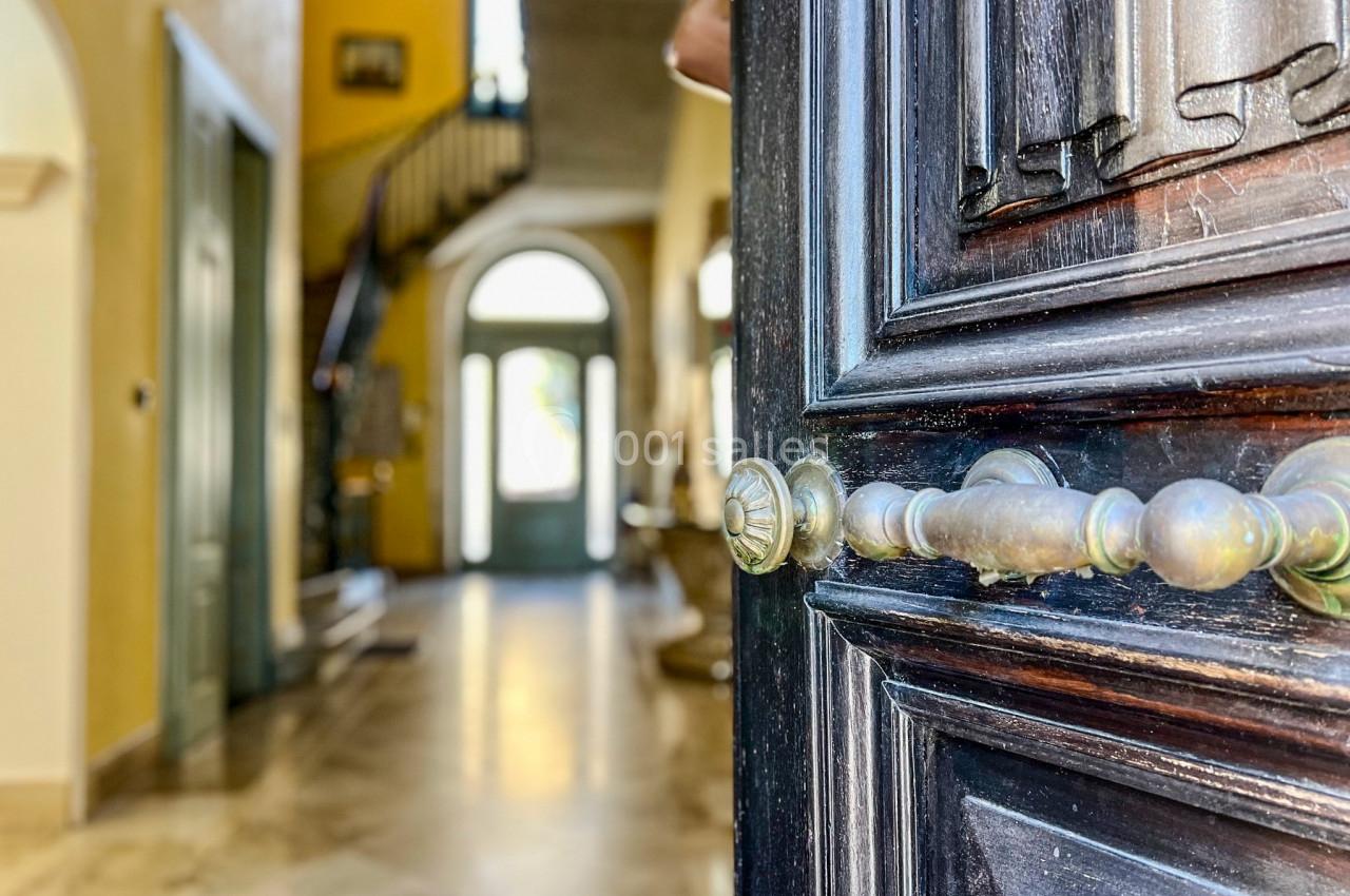 Porte en bois sombre entrouverte donnant sur un hall lumineux avec escalier et sol en marbre.