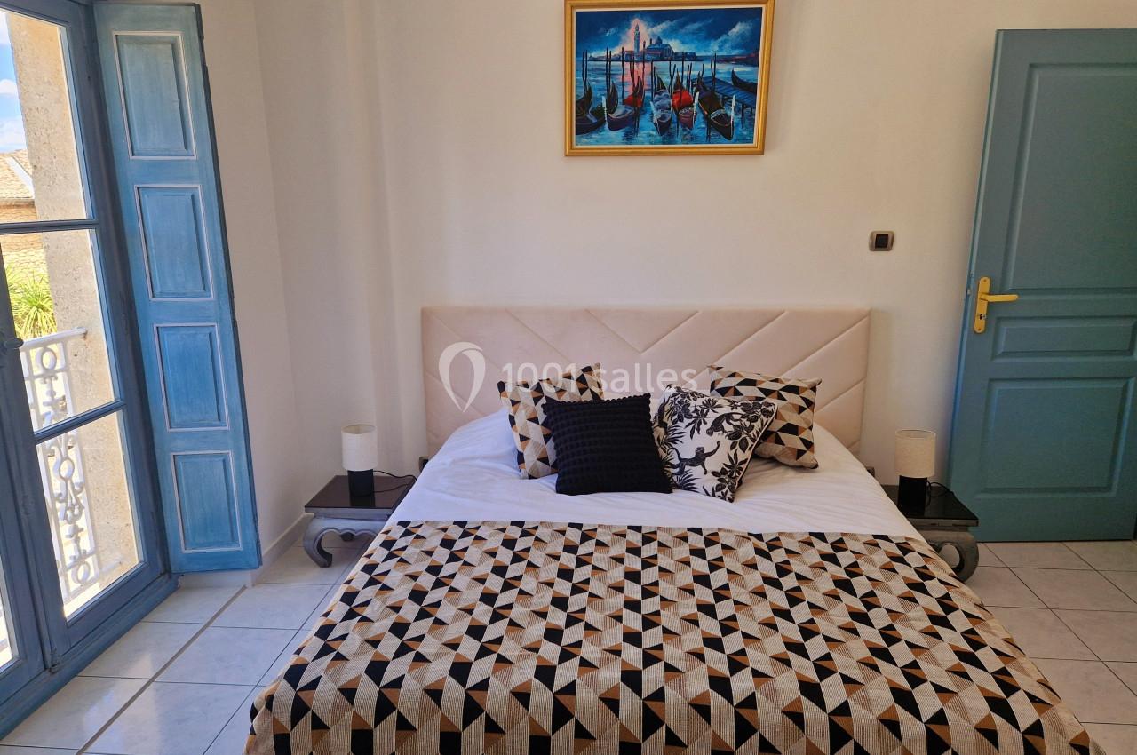 Chambre lumineuse avec lit double, couvre-lit géométrique, tableau mural et fenêtres ouvertes sur l'extérieur.