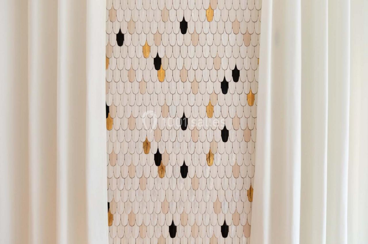 Motif mural en écailles beige, noir et doré, encadré par des rideaux blancs.