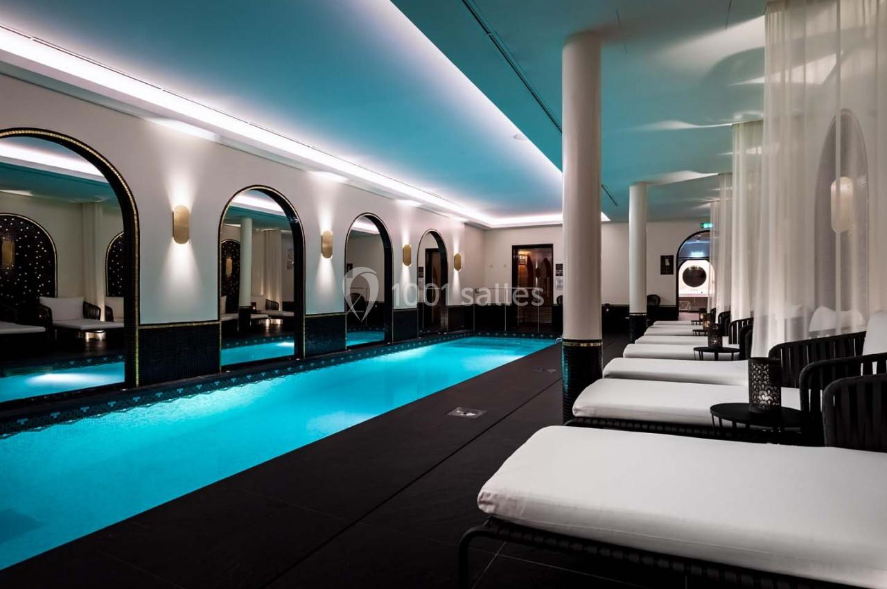 Piscine intérieure élégante avec éclairage tamisé, chaises longues blanches et arches décoratives en arrière-plan.