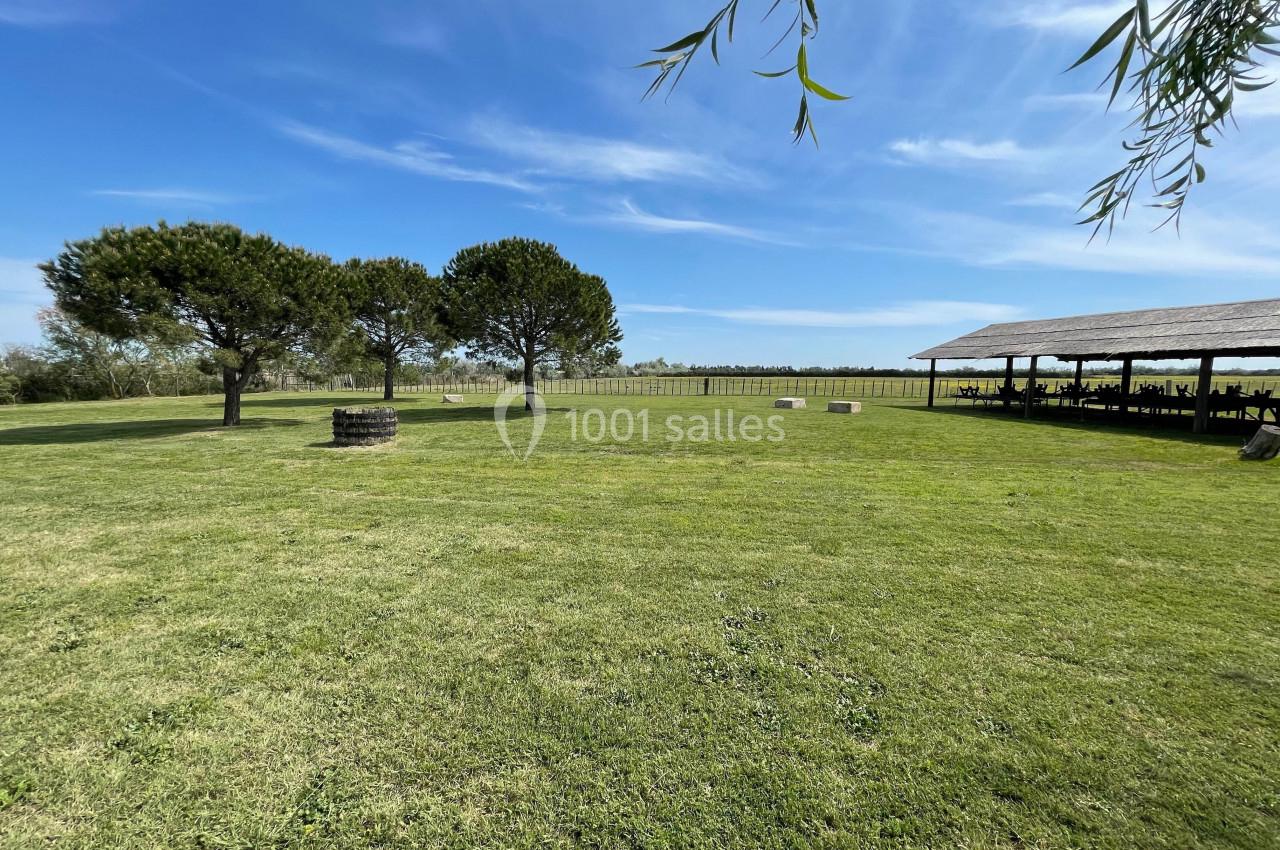 Grand espace vert avec des arbres, une clôture en arrière-plan et une structure couverte sur la droite.