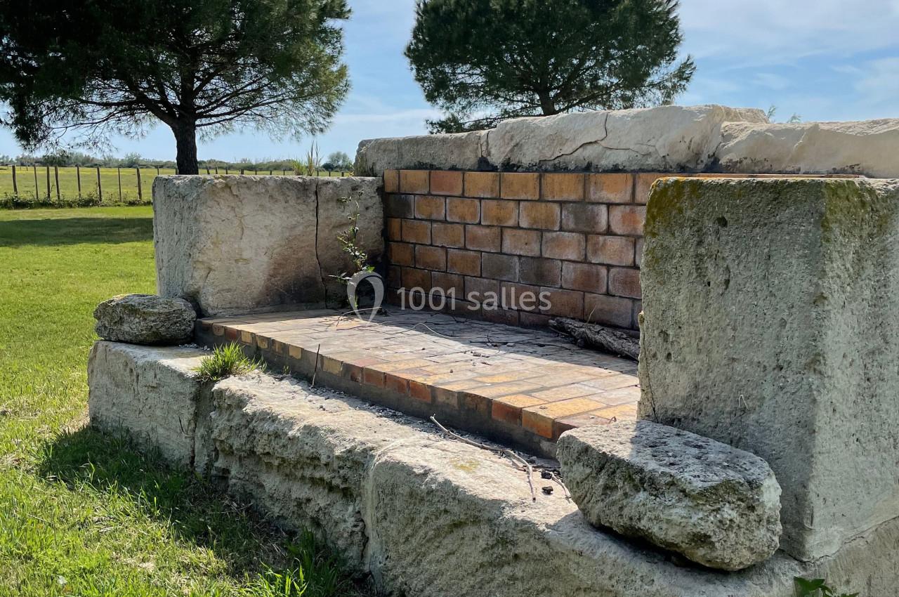 Barbecue en pierre et briques dans un jardin, entouré de pelouse et d'arbres sous un ciel dégagé.