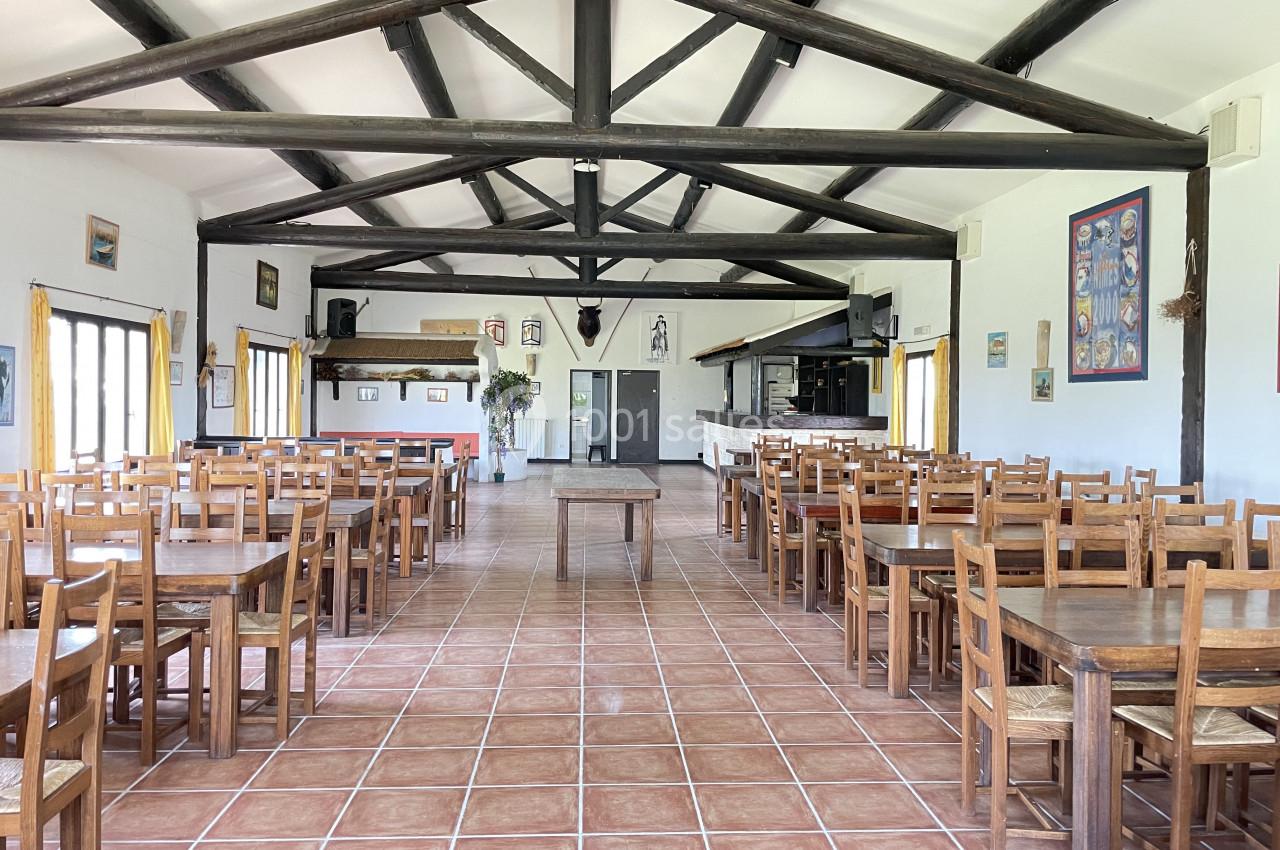 Salle spacieuse avec des tables et des chaises en bois, carrelage au sol et poutres apparentes au plafond.