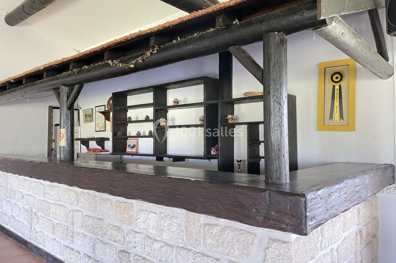 Comptoir en bois sombre avec étagères décoratives, encadré par une structure en poutres et un mur en pierre.