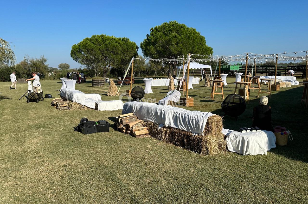 Espace extérieur aménagé avec bottes de foin recouvertes de tissus blancs, tables hautes et guirlandes lumineuses.