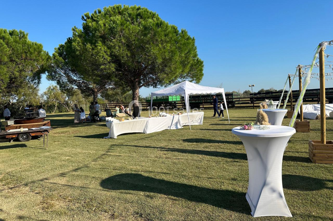 Tables dressées et tonnelle blanche installées sur une pelouse pour un événement en extérieur sous un ciel dégagé.