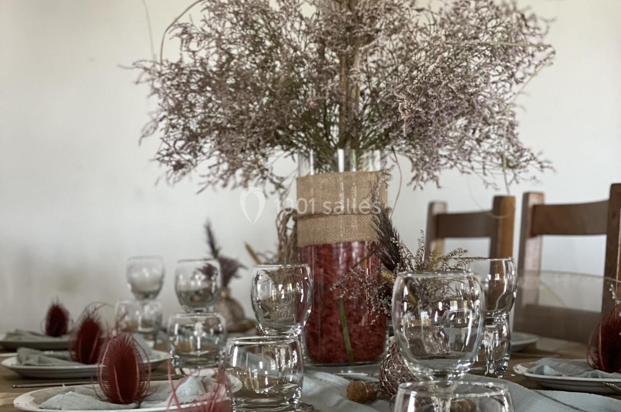 Table dressée avec des assiettes, verres et serviettes, décorée de plumes rouges et d'un bouquet de fleurs séchées.