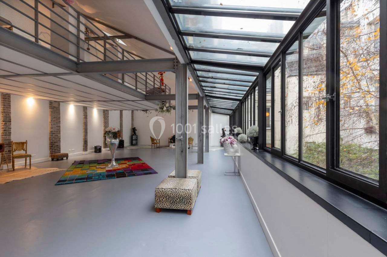 Intérieur lumineux avec verrière, mezzanine, murs en briques et mobilier éclectique dans un espace ouvert.
