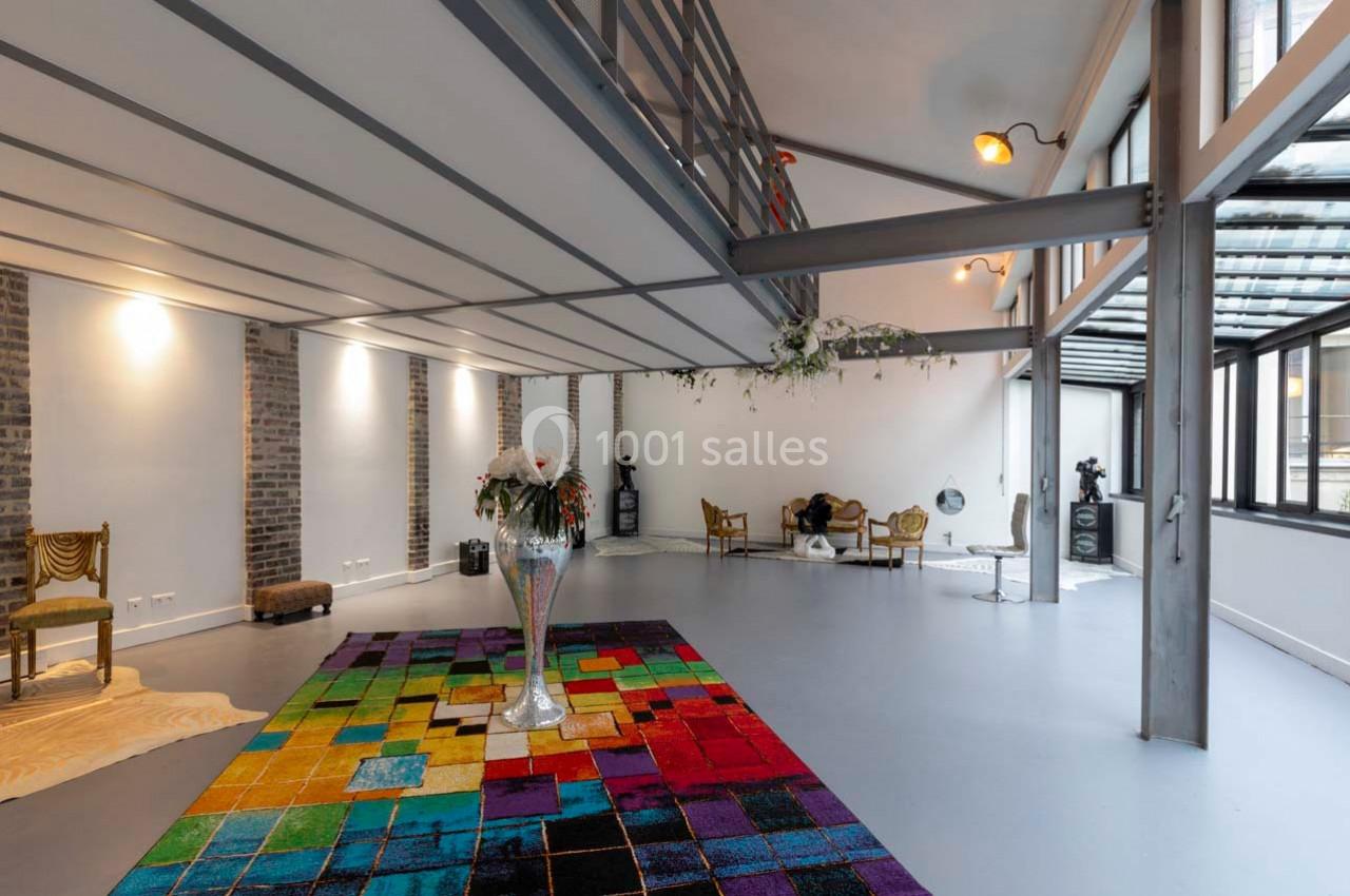 Espace intérieur lumineux avec un sol gris, un tapis coloré, des meubles éclectiques et une grande baie vitrée.