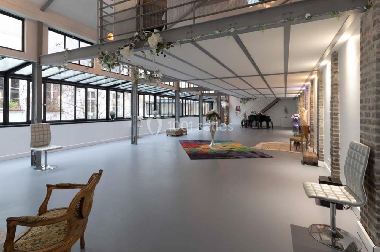 Grand espace lumineux avec des murs en briques, des baies vitrées, un tapis coloré et des chaises disposées.