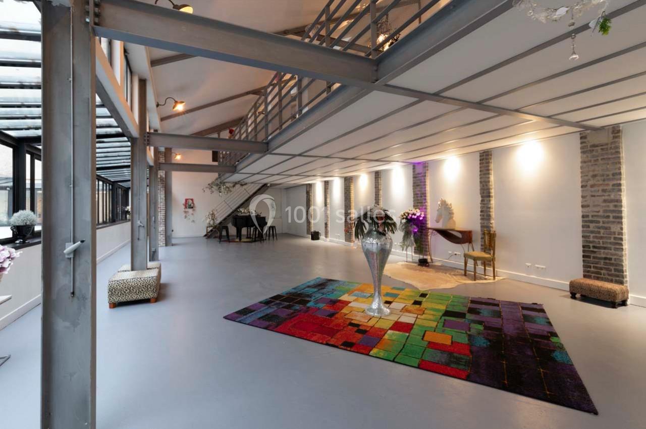 Intérieur spacieux et lumineux avec mezzanine, murs en briques, tapis coloré et mobilier moderne.