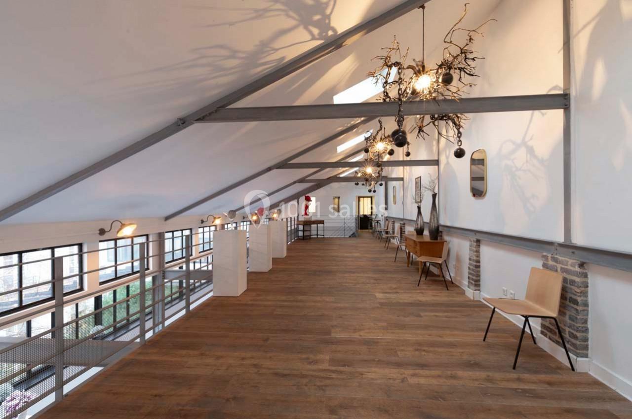 Intérieur d'un espace lumineux avec parquet, mobilier minimaliste et éclairage suspendu, sous une charpente apparente.