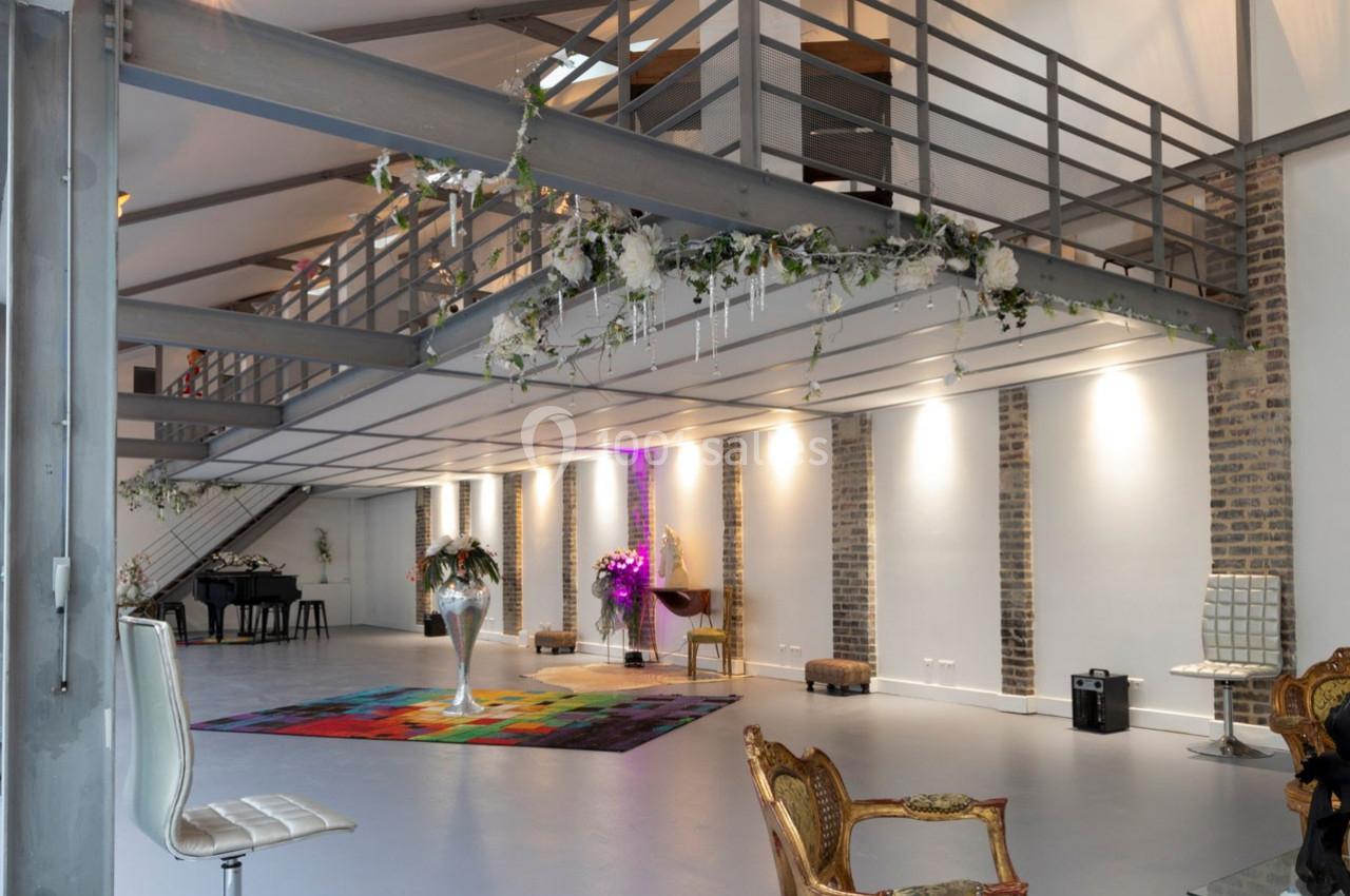 Salle spacieuse avec mezzanine, murs en briques, décoration florale suspendue, mobilier éclectique et lumière naturelle.