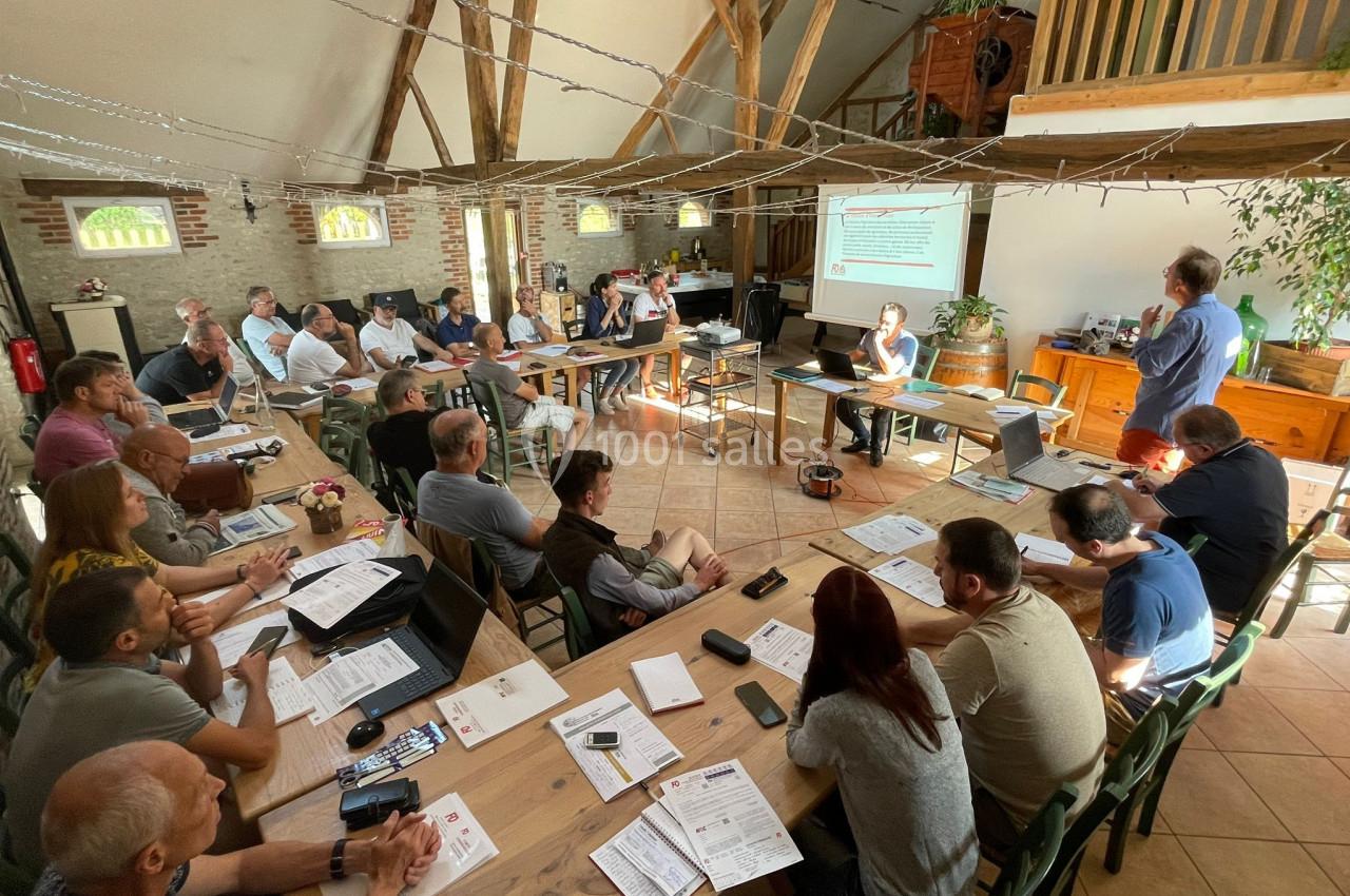 Groupe de personnes assistant à une présentation dans une salle avec poutres apparentes et écran de projection.
