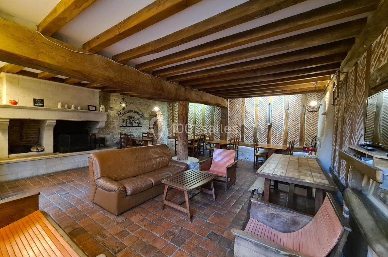 Salle de séjour rustique avec poutres apparentes, cheminée, mobilier en bois et sol en carrelage.