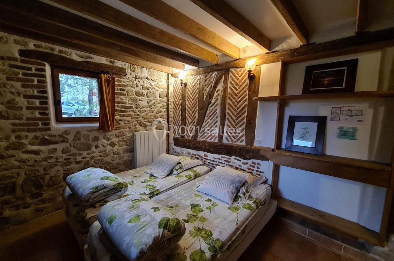 Chambre rustique avec murs en pierre, poutres apparentes, lit double et petite fenêtre donnant sur l'extérieur.