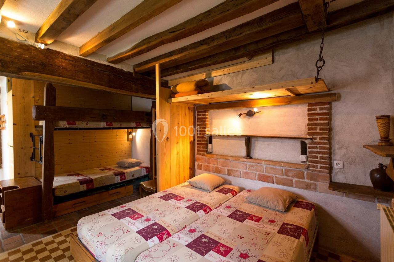 Chambre rustique avec lits jumeaux, lits superposés en bois, murs en briques et poutres apparentes.