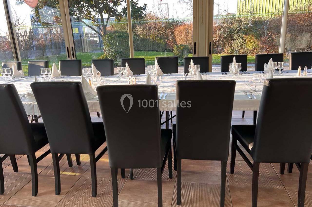 Salle lumineuse avec une grande table dressée, entourée de chaises noires, donnant sur un jardin extérieur.