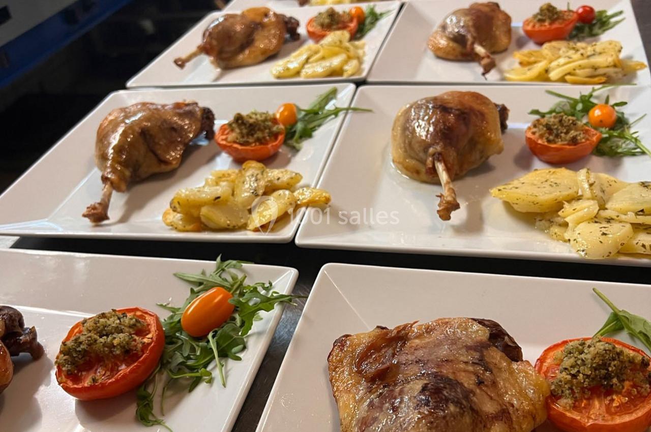 Assiettes de confit de canard servies avec pommes de terre, tomates farcies et roquette sur des plats blancs.