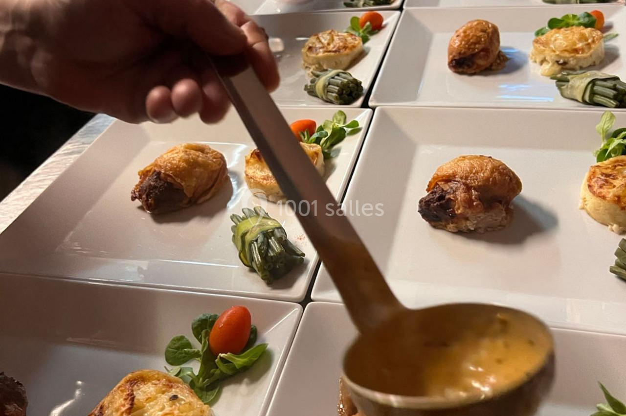 Service en cours de plats gastronomiques avec sauce versée sur des assiettes contenant viande, légumes et garnitures.