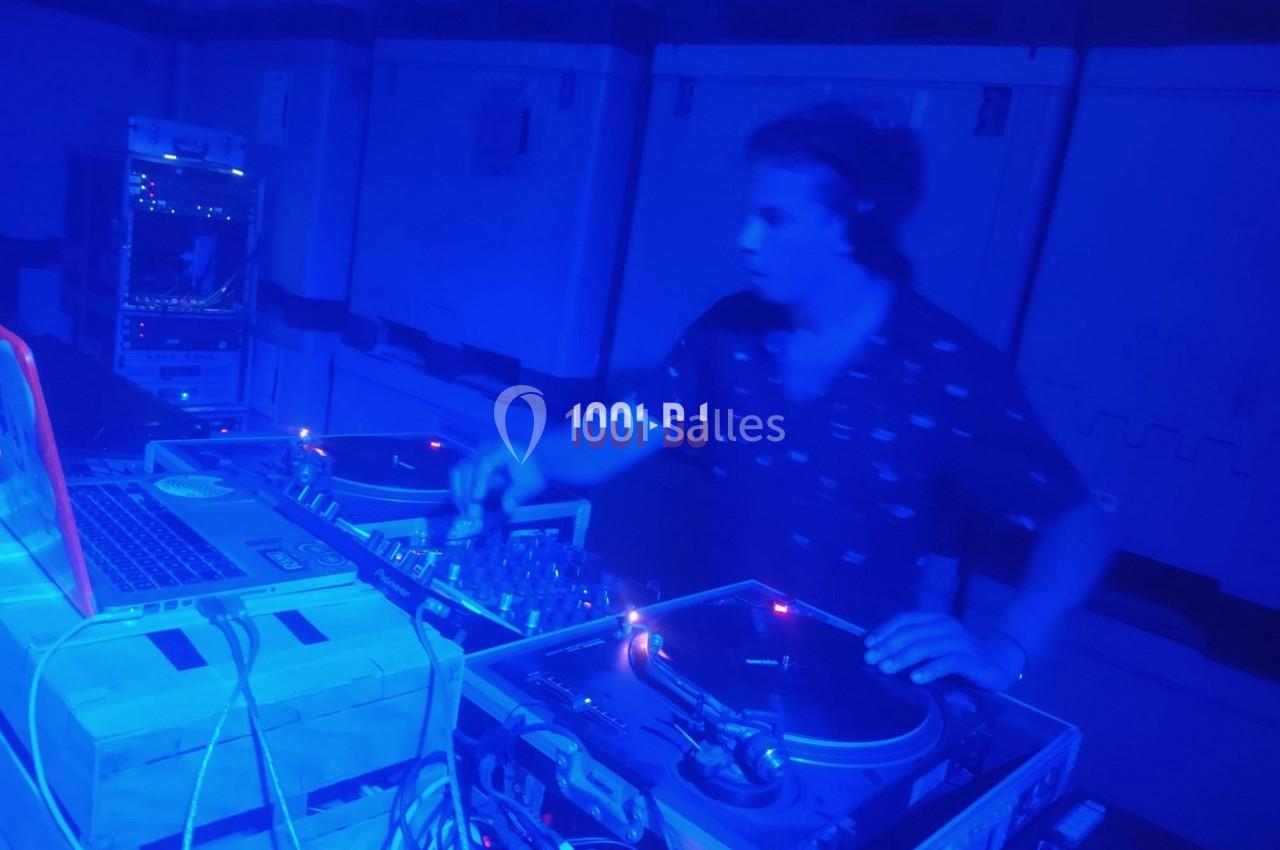 Un DJ mixe de la musique sur des platines dans une ambiance lumineuse bleue.
