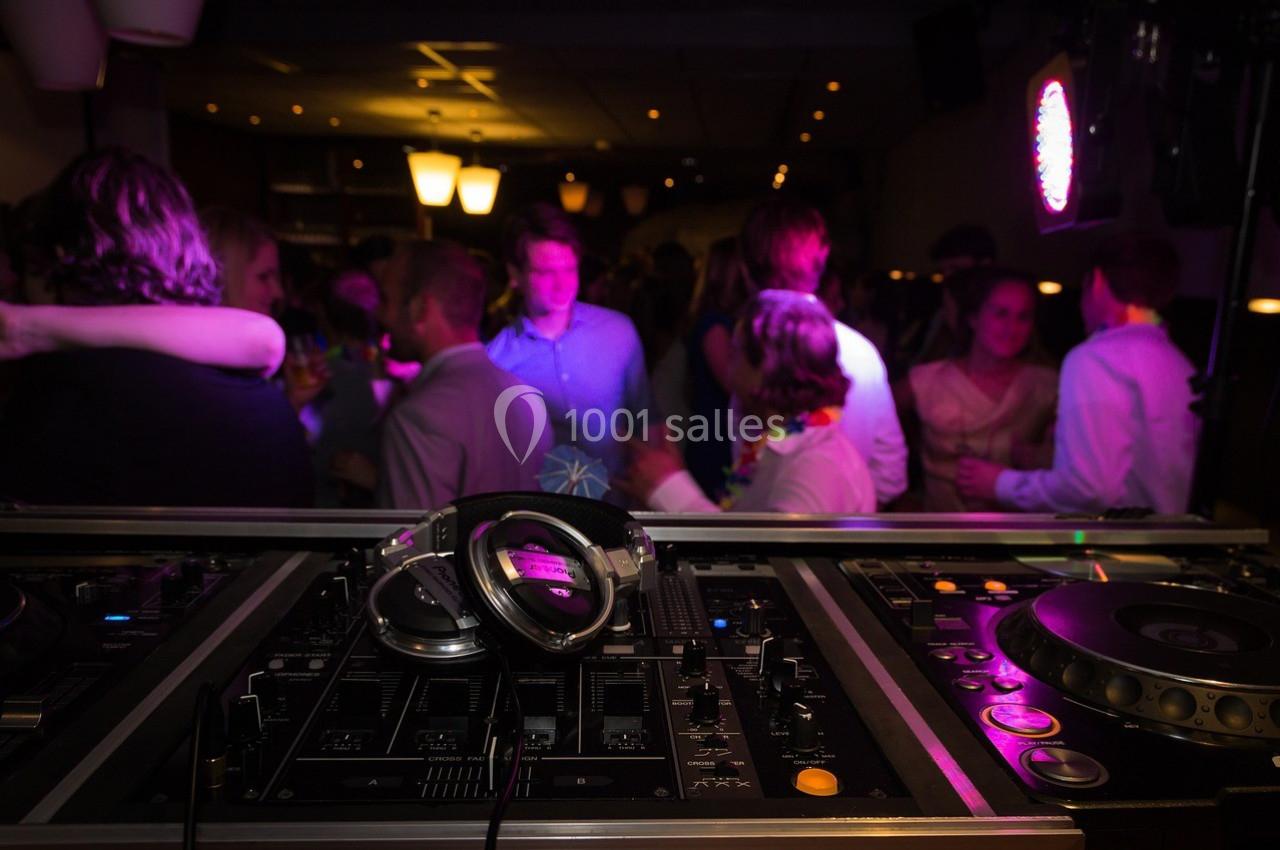 Vue d'une table de mixage avec des casques audio au premier plan, et une foule dansante en arrière-plan.