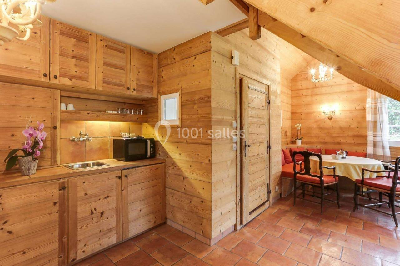 Cuisine en bois clair avec évier, micro-ondes, orchidée sur le plan de travail et coin repas avec table et chaises.
